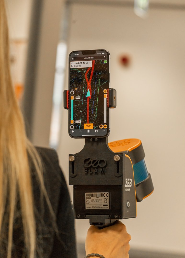 Photo showing a surveyor using a handheld LiDAR scanner (GeoSLAM) while walking through an office interior, demonstrating the portability and speed of interior scanning